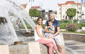 Eine Familie sitzt l&auml;chelnd an einem Brunnen auf dem Tullner Hauptplatz.