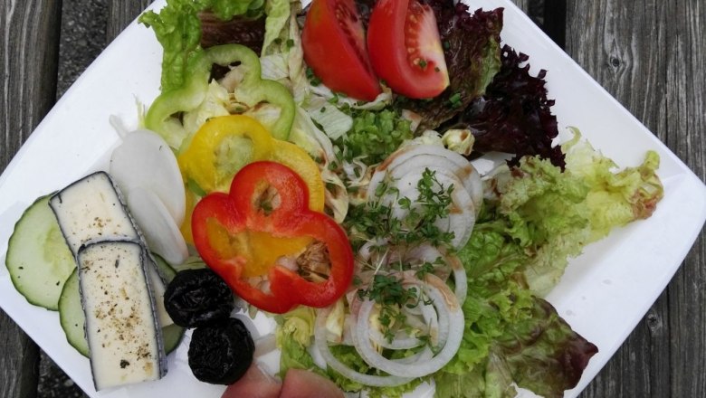 Ein Teller mit Salat, Tomaten, Paprika, Zwiebeln, Schinken und Käse auf einem Holztisch.