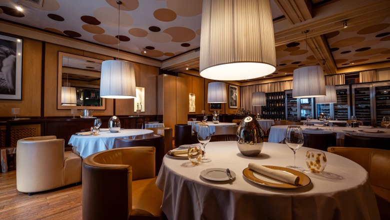 Elegantes Restaurant mit runden Tischen, wei&szlig;en Tischdecken und gro&szlig;en, h&auml;ngenden Lampen.