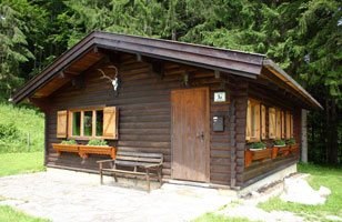 Jagdhaus, © Archiv Ein kleines, rustikales Jagdhaus aus Holz mit Fensterläden und Geweih an der Fassade, umgeben von Wald.