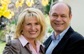 Ein lächelndes Paar steht draußen vor einem Hintergrund mit gelben Blättern.