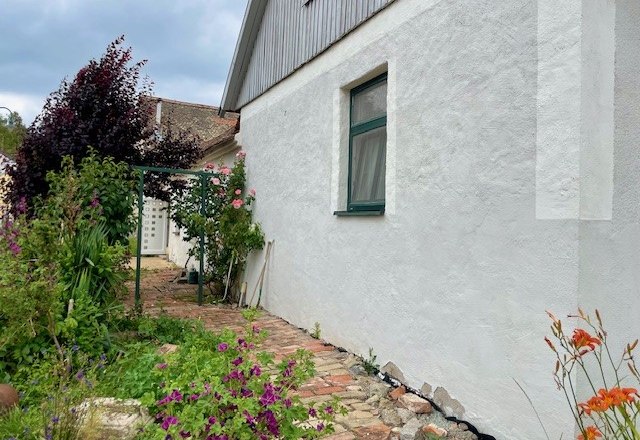 Au&szlig;enansicht eines Hauses mit wei&szlig;er Wand, Garten und Blumen.