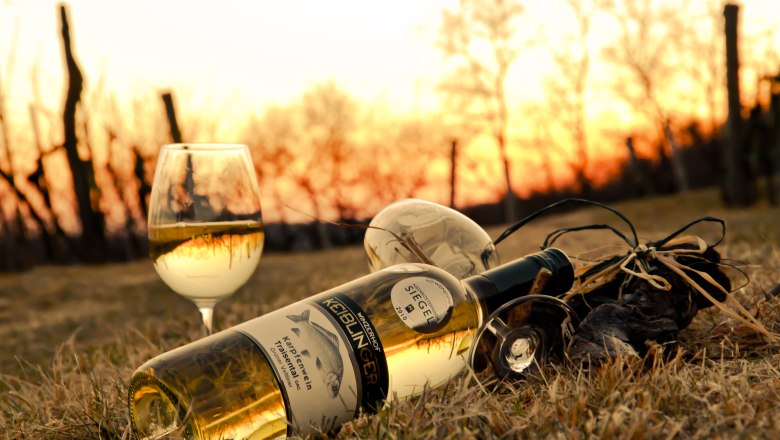 Weinflasche und Glas im Gras bei Sonnenuntergang.