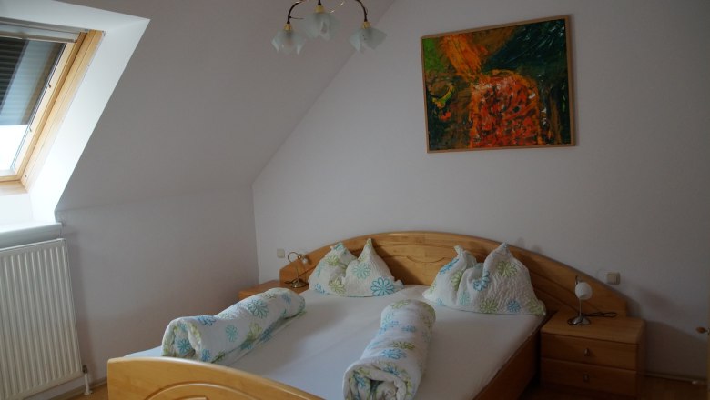 Schlafzimmer mit Doppelbett, Dachfenster und abstraktem Gem&auml;lde an der Wand.