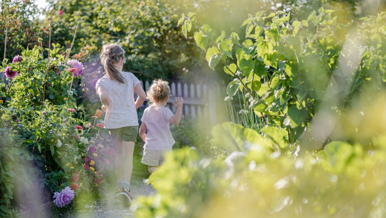 Zwei Kinder laufen durch einen bl&uuml;henden Gartenweg.