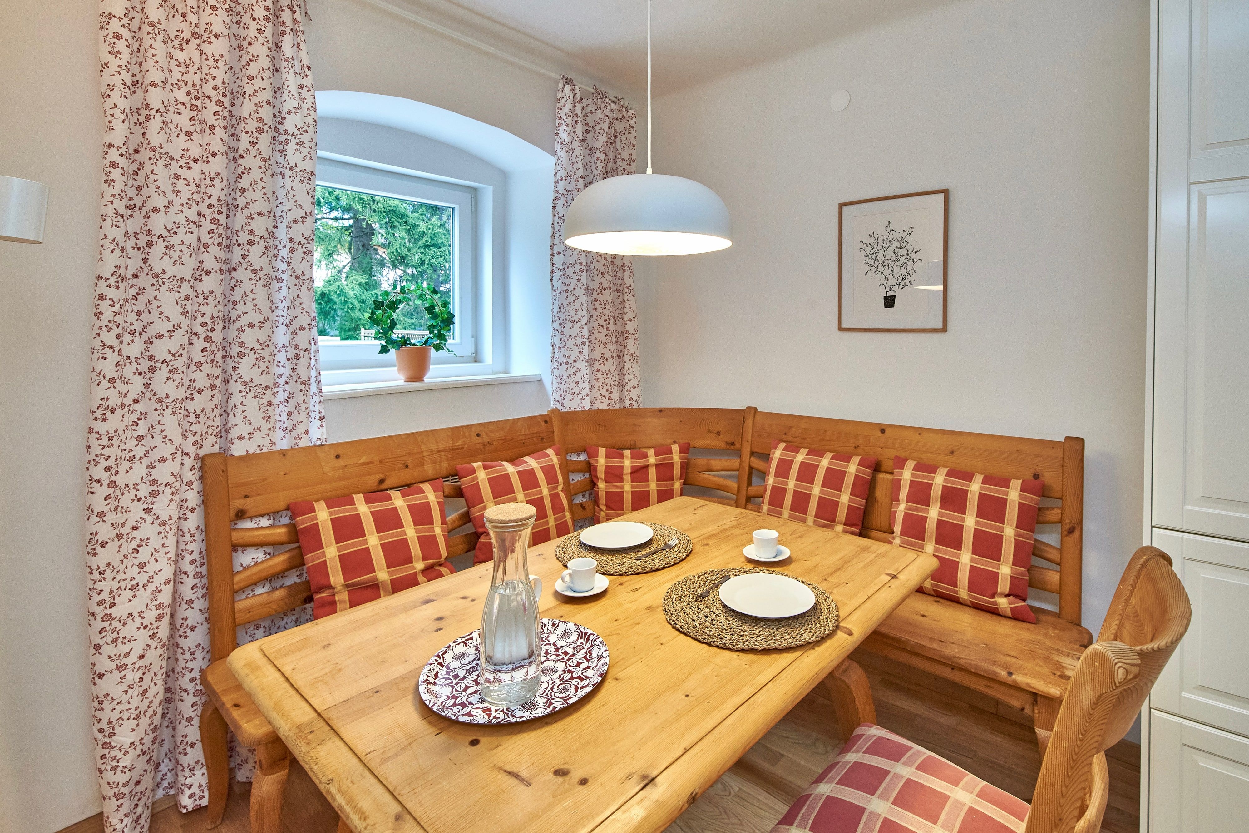 Gemütlicher Essbereich mit Holztisch, Eckbank und karierten Kissen.