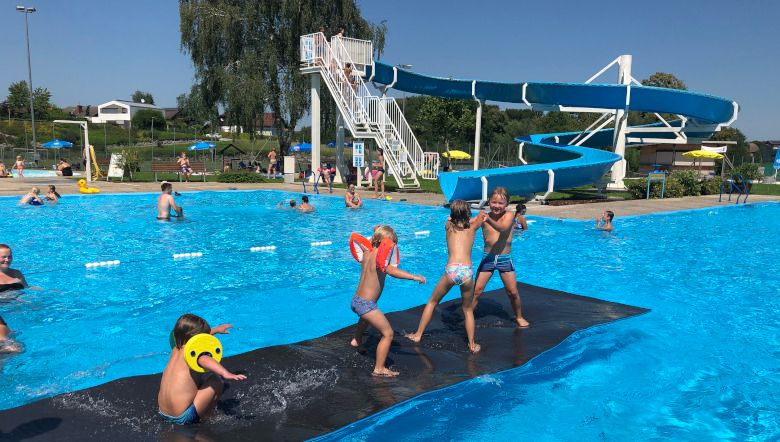 Kinder spielen im Freibad Neuhofen an der Ybbs auf einer schwimmenden Matte vor einer Wasserrutsche.