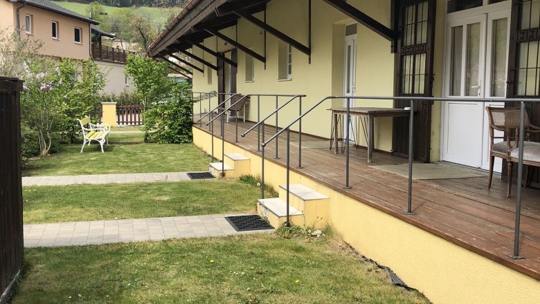 Au&szlig;enansicht eines gelben Geb&auml;udes mit Veranda und Berg im Hintergrund.