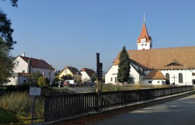 Pfarr- und Wallfahrtskirche Droß mit umliegenden Gebäuden und blauem Himmel.