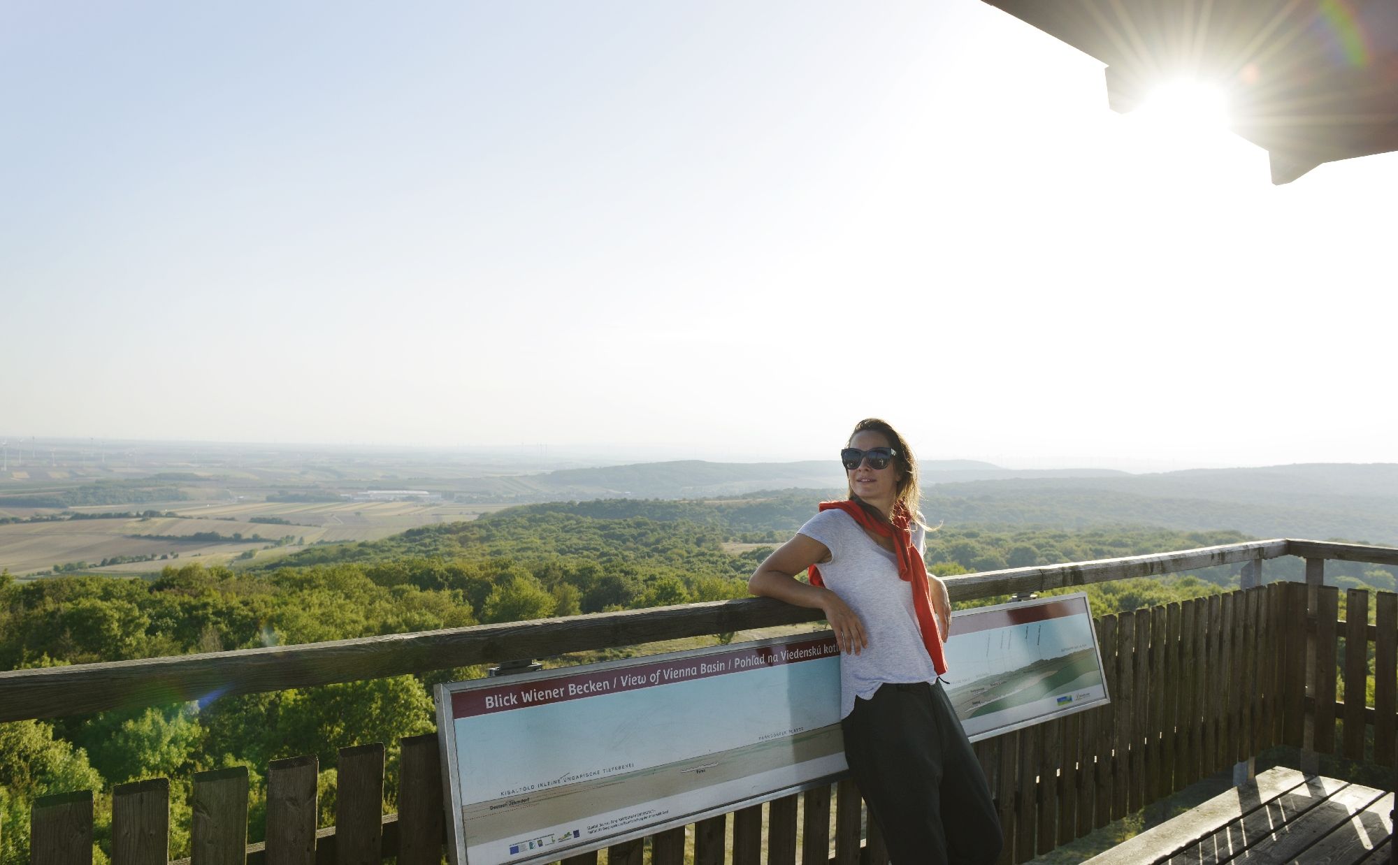 Frau steht auf einer Aussichtsplattform mit Blick auf eine weite Landschaft.