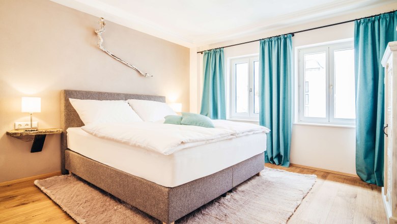 Modernes Schlafzimmer mit grauem Bett, blauen Vorh&auml;ngen und Holzdekor.