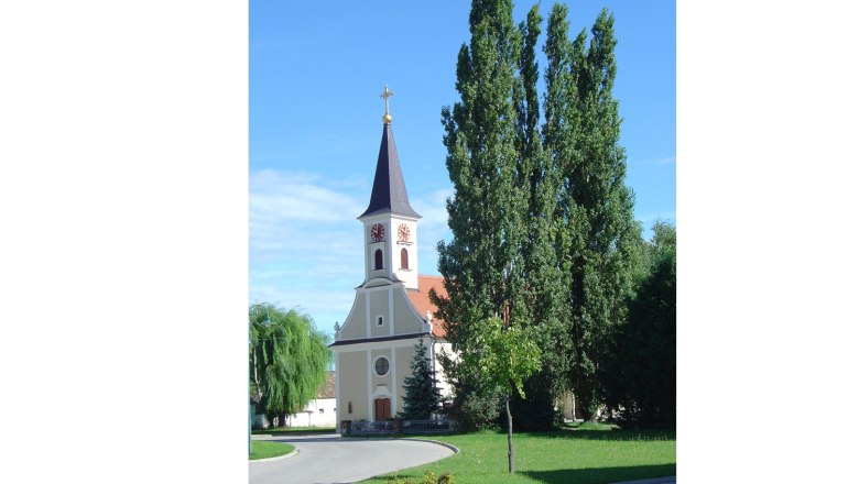 Eine Kirche mit Turm und Uhr vor blauem Himmel, umgeben von Bäumen.