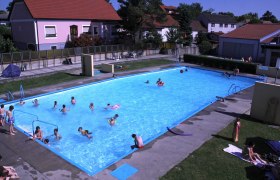 Ein Freibad mit mehreren Menschen im Wasser und auf der Liegewiese.