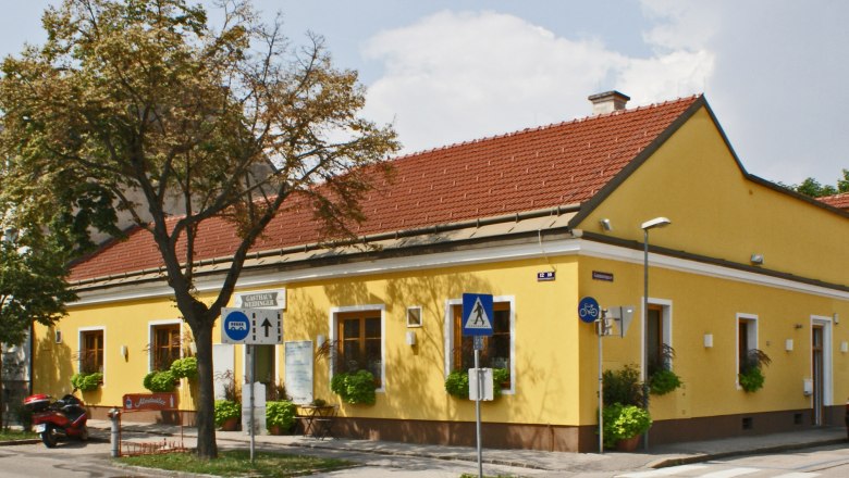 Gelbes Geb&auml;ude mit rotem Dach, beschildert als Gasthaus Weidinger, an einer Stra&szlig;enecke mit Zebrastreifen und Verkehrsschildern.