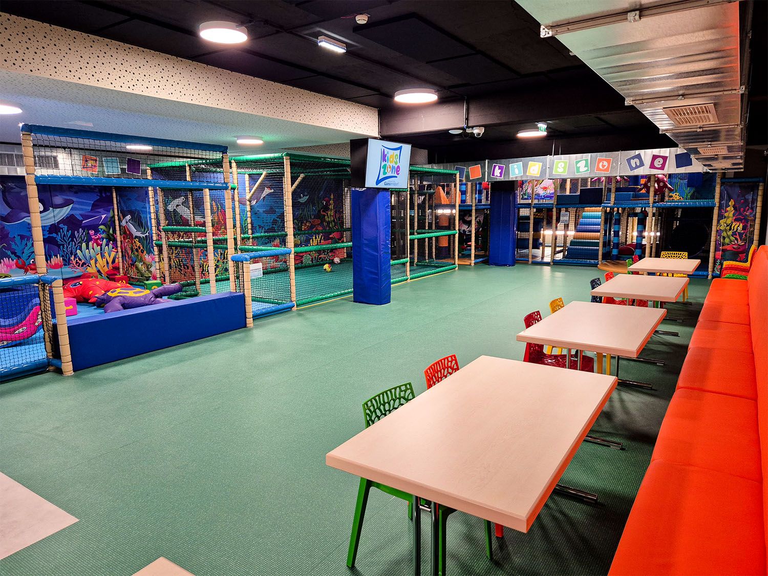 Innenansicht eines bunten Indoor-Spielplatzes mit Klettergerüsten und Tischen.