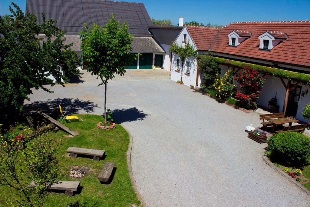 Ein gepflegter Innenhof mit Bäumen, Blumen und Sitzgelegenheiten, umgeben von Gebäuden mit roten Dächern.