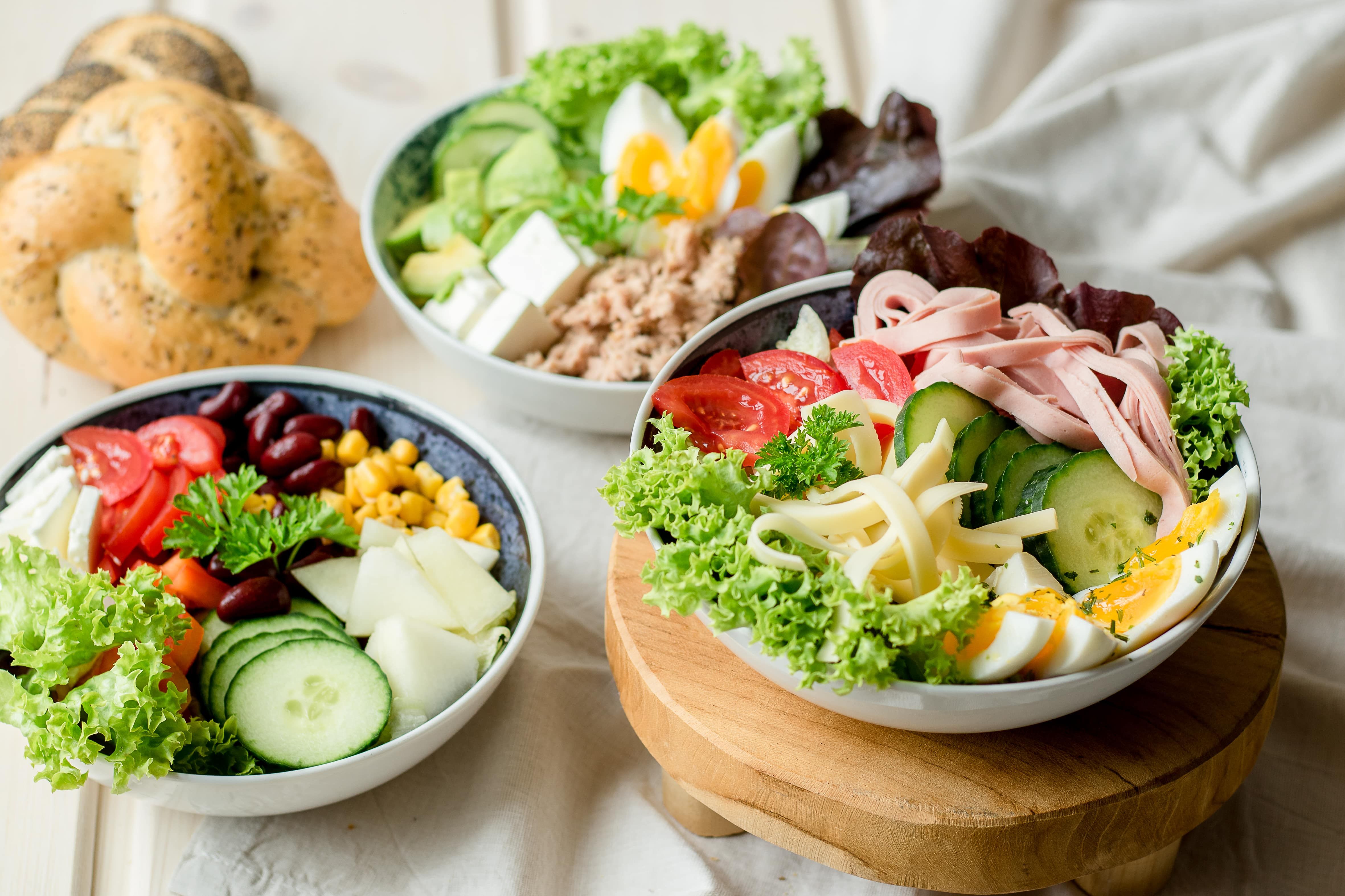 Drei Schalen mit frischen Salaten, Gemüse und Eiern auf einem Tisch.