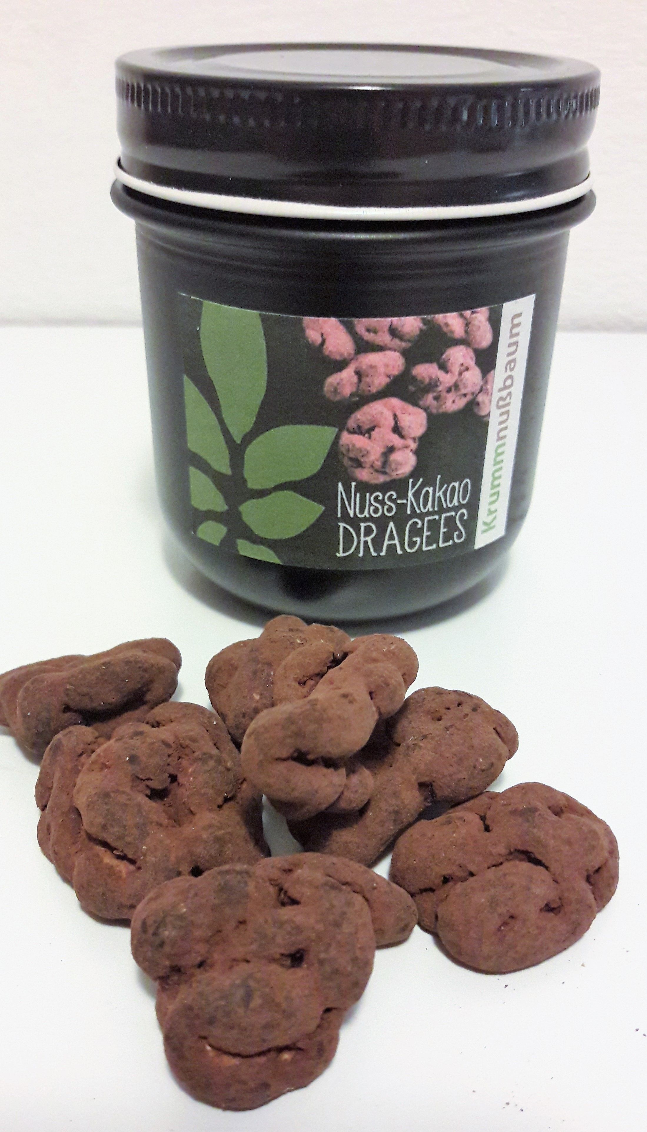 Ein Glas mit der Aufschrift 'Nuss-Kakao Dragees' und einige Dragees davor.