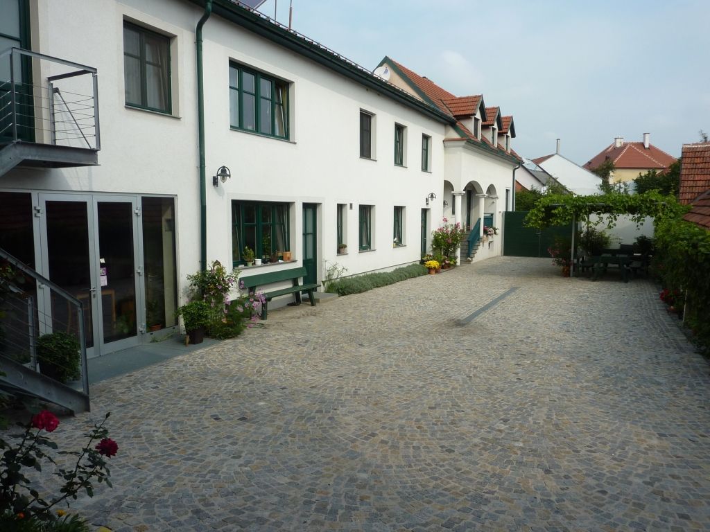 Innenhof eines Weinguts mit gepflastertem Boden, weißen Gebäuden und grünen Fensterrahmen.