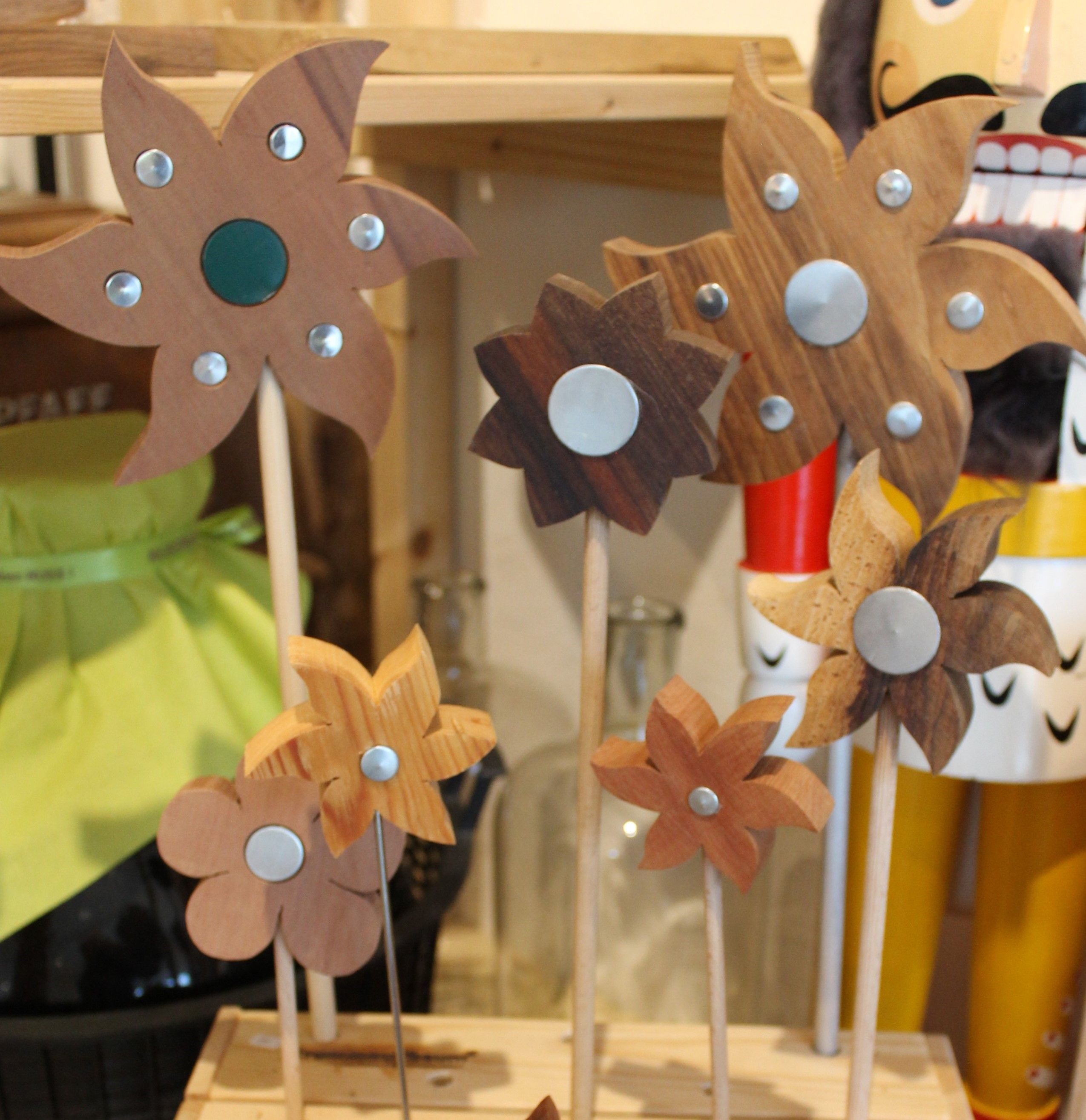 Holzblumen mit Metallverzierungen auf Stäben in einem Regal.