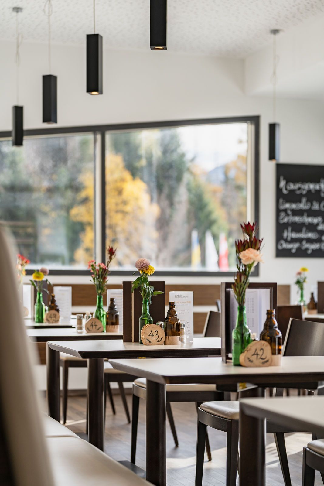 Innenansicht eines modernen Bistros mit Tischen, Blumenvasen und Menütafeln.