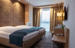 Modernes Hotelzimmer mit Doppelbett, Holzverkleidung und Fenster mit Vorhängen.