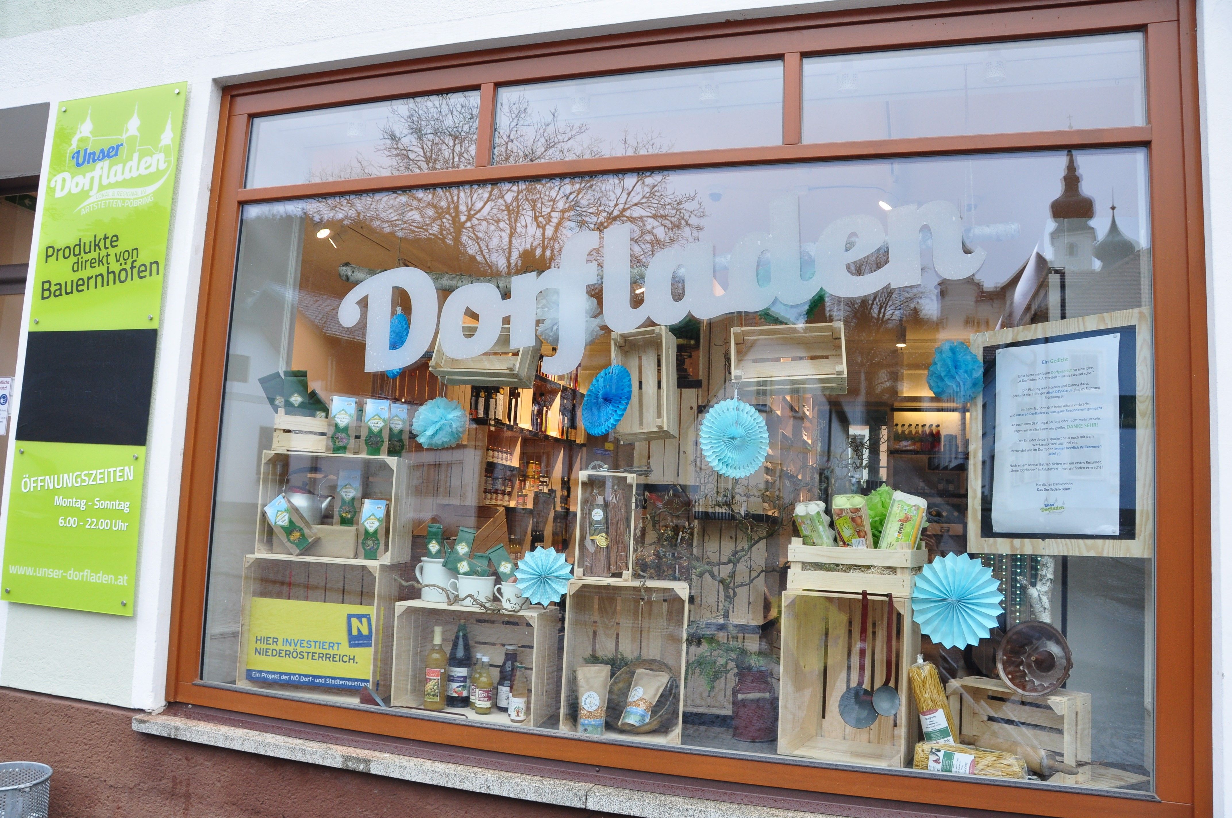 Schaufenster eines Dorfladens mit Produkten und Dekorationen.