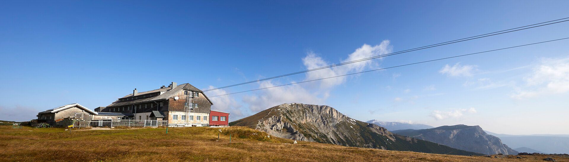 Panoramablick auf einen Berghütte mit umliegenden Gipfeln unter blauem Himmel.