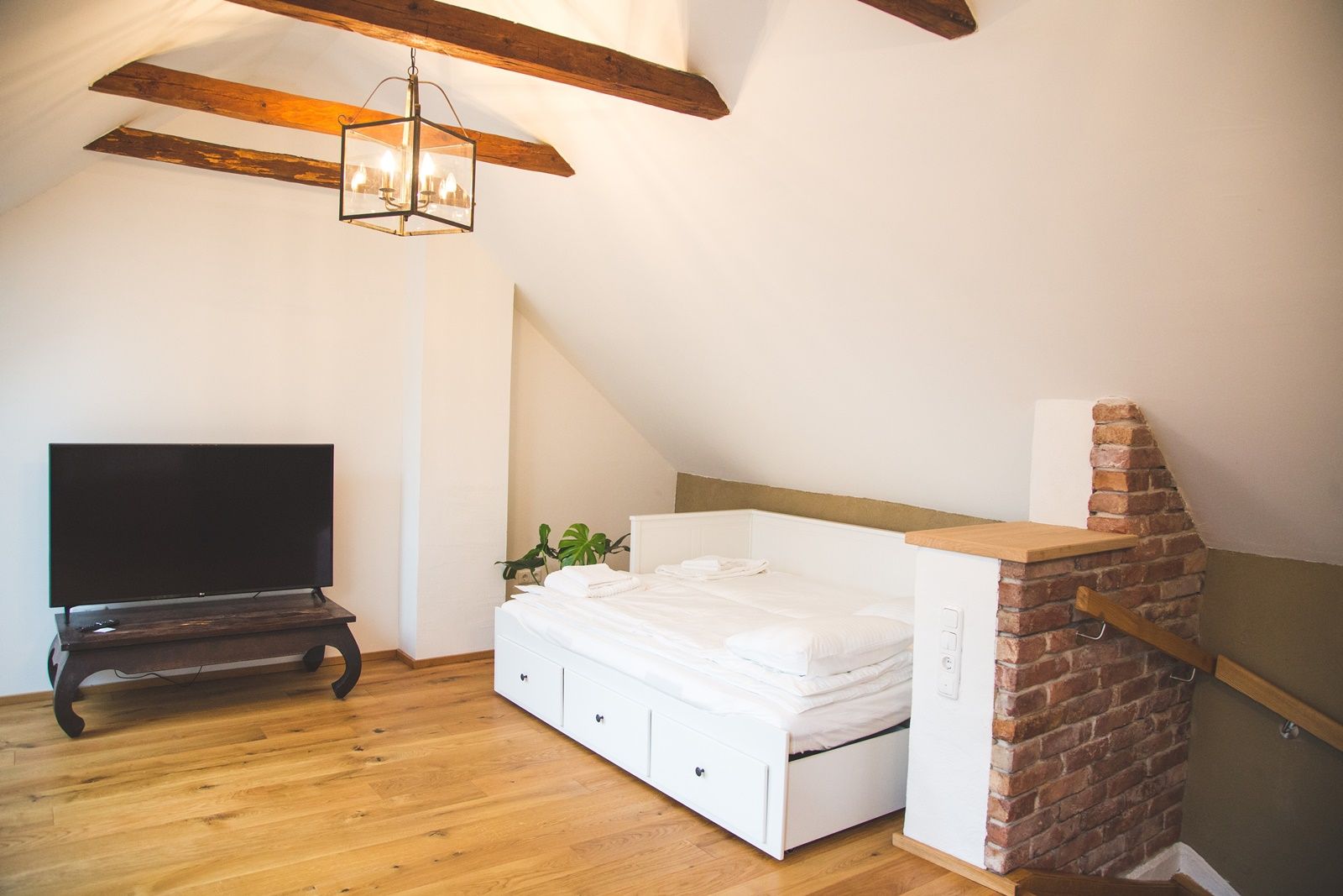 Ein Dachzimmer mit Holzboden, einem weißen Bett, einem Fernseher auf einem Tisch und freiliegenden Holzbalken an der Decke.