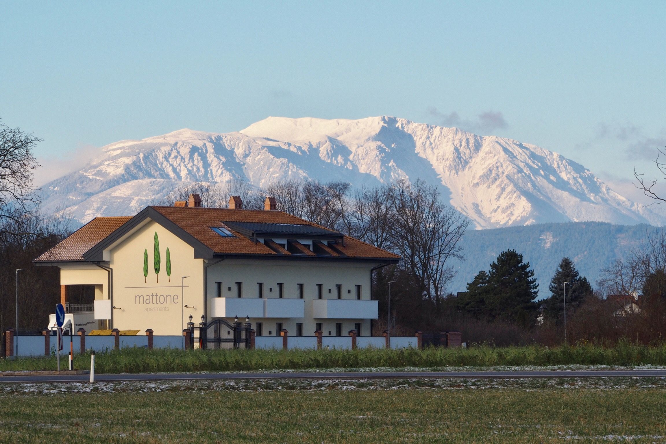 Gebäude mit der Aufschrift 'mattone apartments' vor schneebedecktem Berg im Hintergrund.