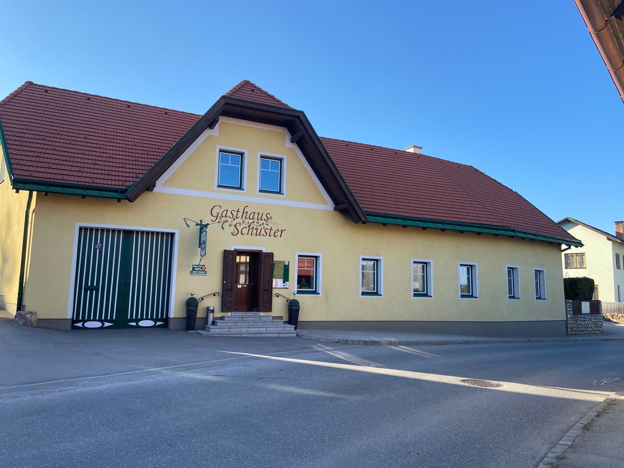 Gelbes Gebäude mit rotem Dach und der Aufschrift 'Gasthaus Schuster'.
