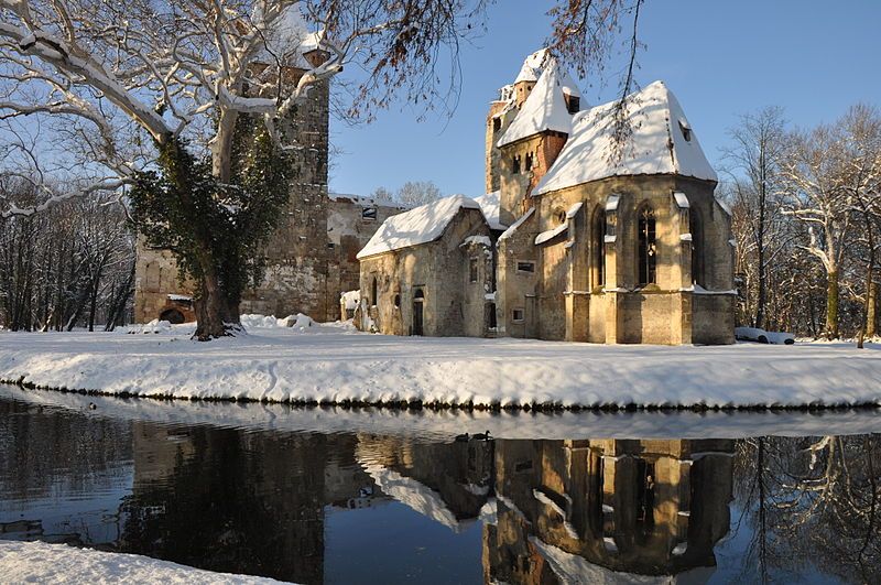 Winterliche Schlossruine Pottendorf mit Schnee und Spiegelung im Wasser.