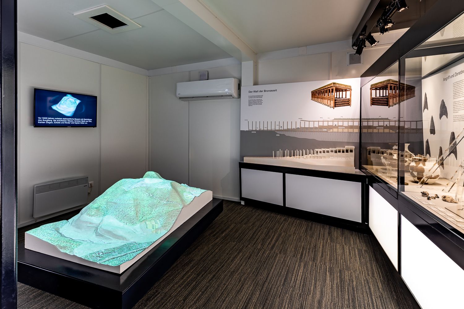 Innenansicht einer Ausstellung im Keltendorf Schwarzenbach mit Modellen und Informationstafeln.