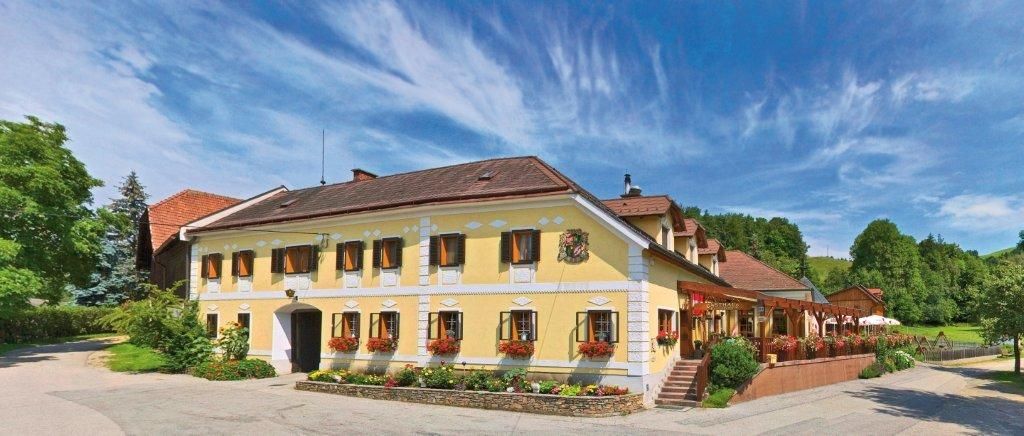 Traditionelles Gasthaus mit gelber Fassade, umgeben von grüner Landschaft und blauem Himmel.