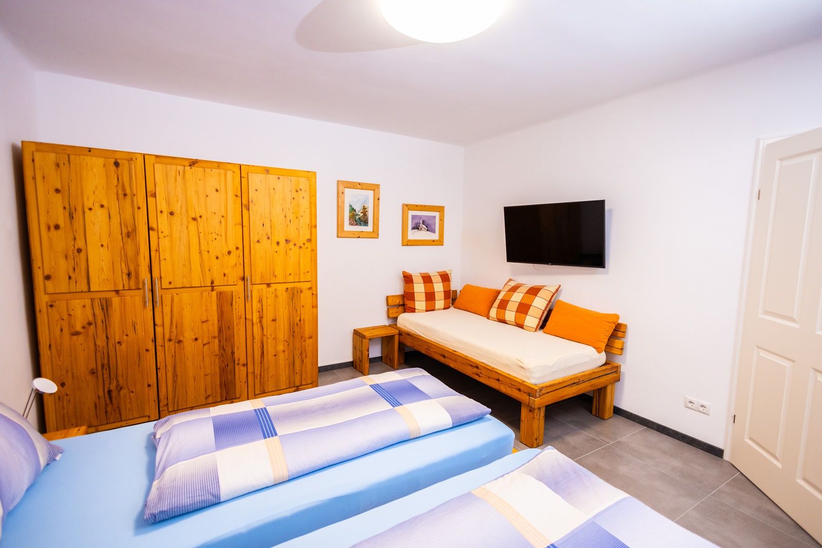 Schlafzimmer mit Holzmöbeln, zwei Betten, Sofa, TV und Bildern an der Wand.