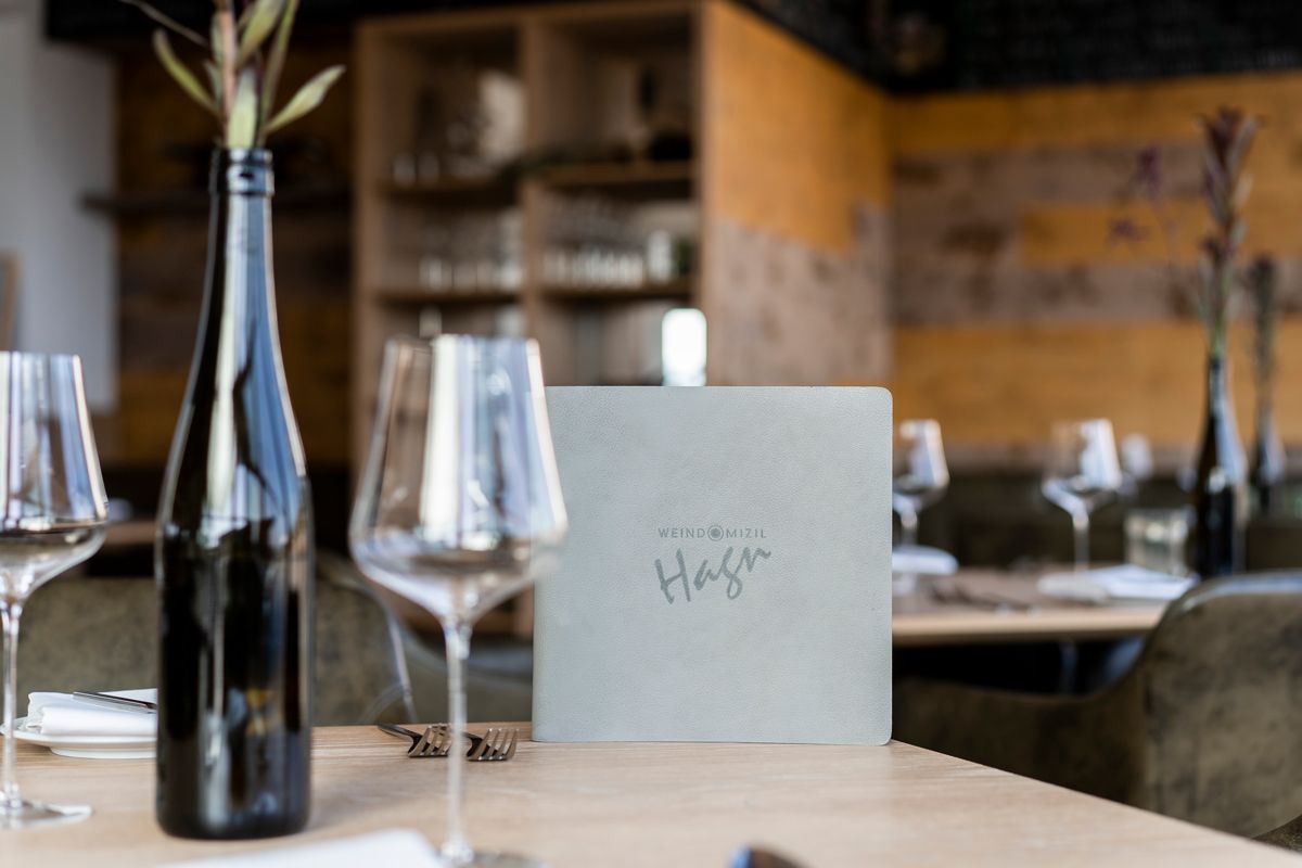 Ein gedeckter Tisch in einem Restaurant mit Weingläsern, einer Weinflasche und einer Speisekarte.