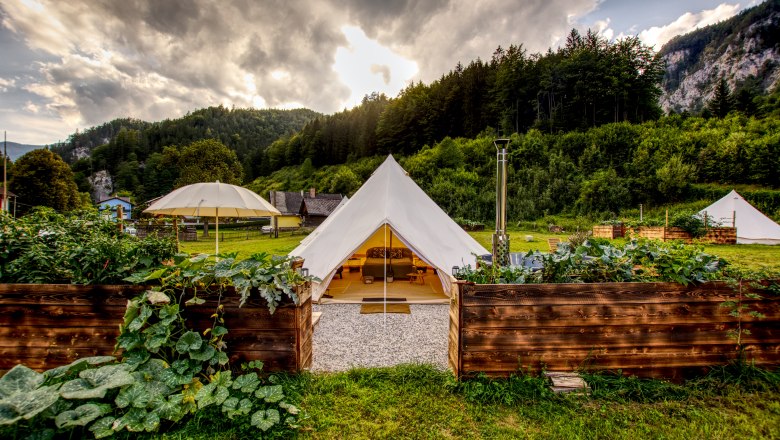 Glamping-Zelt in gr&uuml;ner Landschaft mit Bergen im Hintergrund.