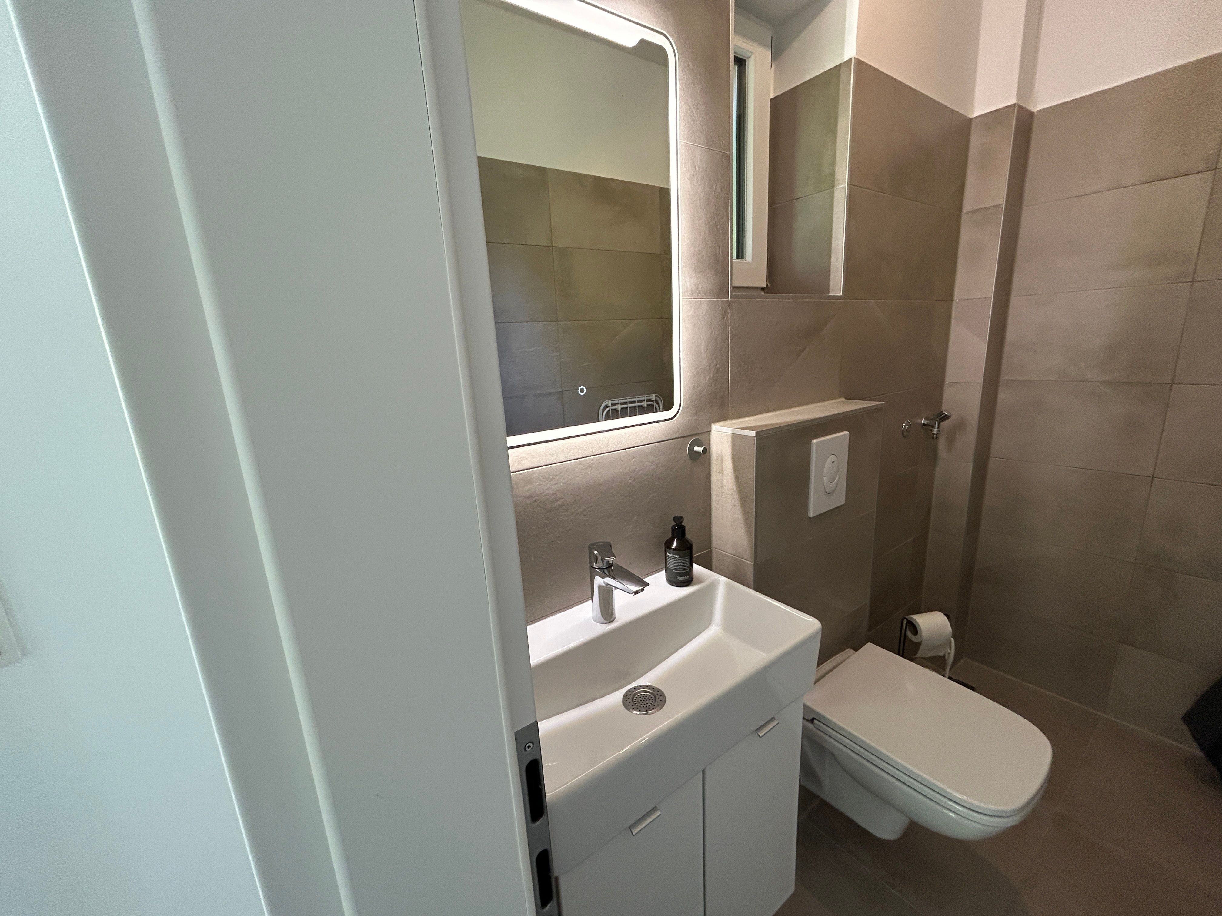 Modernes Badezimmer mit Waschbecken, Spiegel und Toilette.
