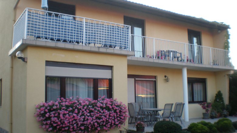 Zweist&ouml;ckiges Haus mit Balkon, Blumen und Gartenm&ouml;beln.