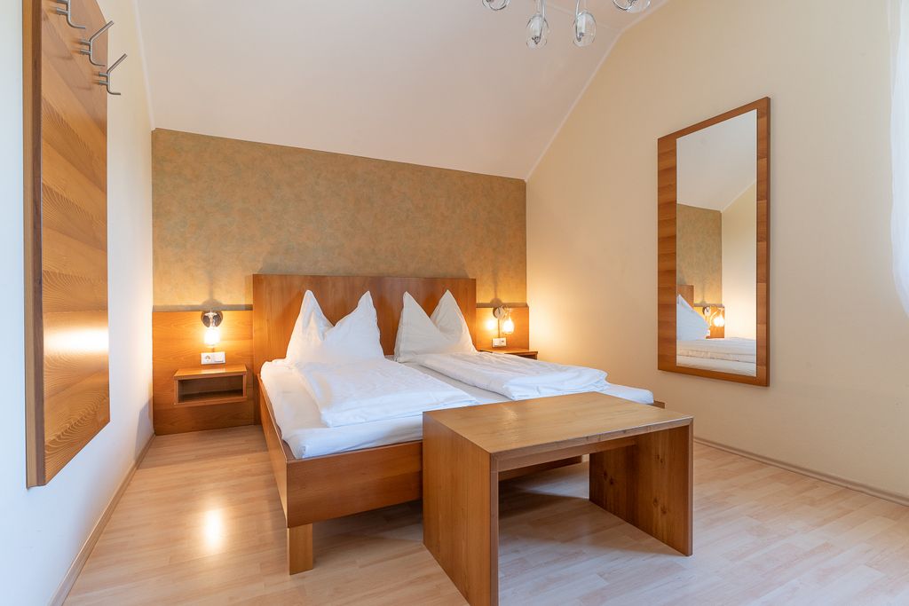 Ein schlicht eingerichtetes Schlafzimmer mit Doppelbett, Holzmöbeln und großem Spiegel.