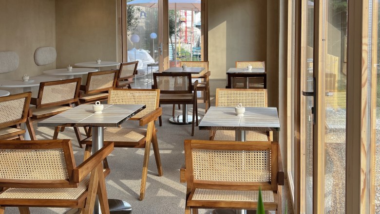 Innenbereich eines Cafés mit Holzmöbeln und großen Fenstern.