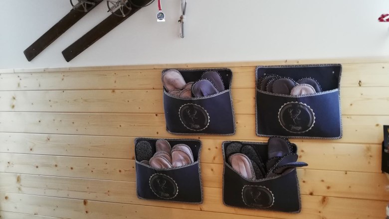 Eingangsbereich mit Holzverkleidung, alten Skiern an der Wand und Filzpantoffeln in Taschen.