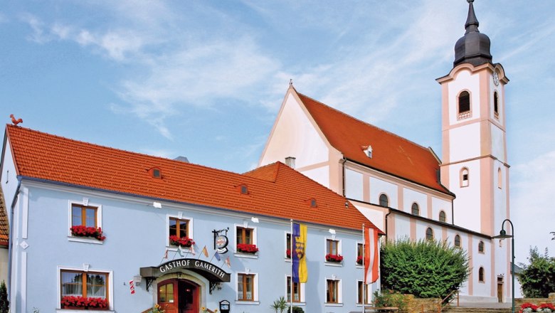 Gasthaus Gamerith neben einer Kirche mit Turm und rotem Dach.