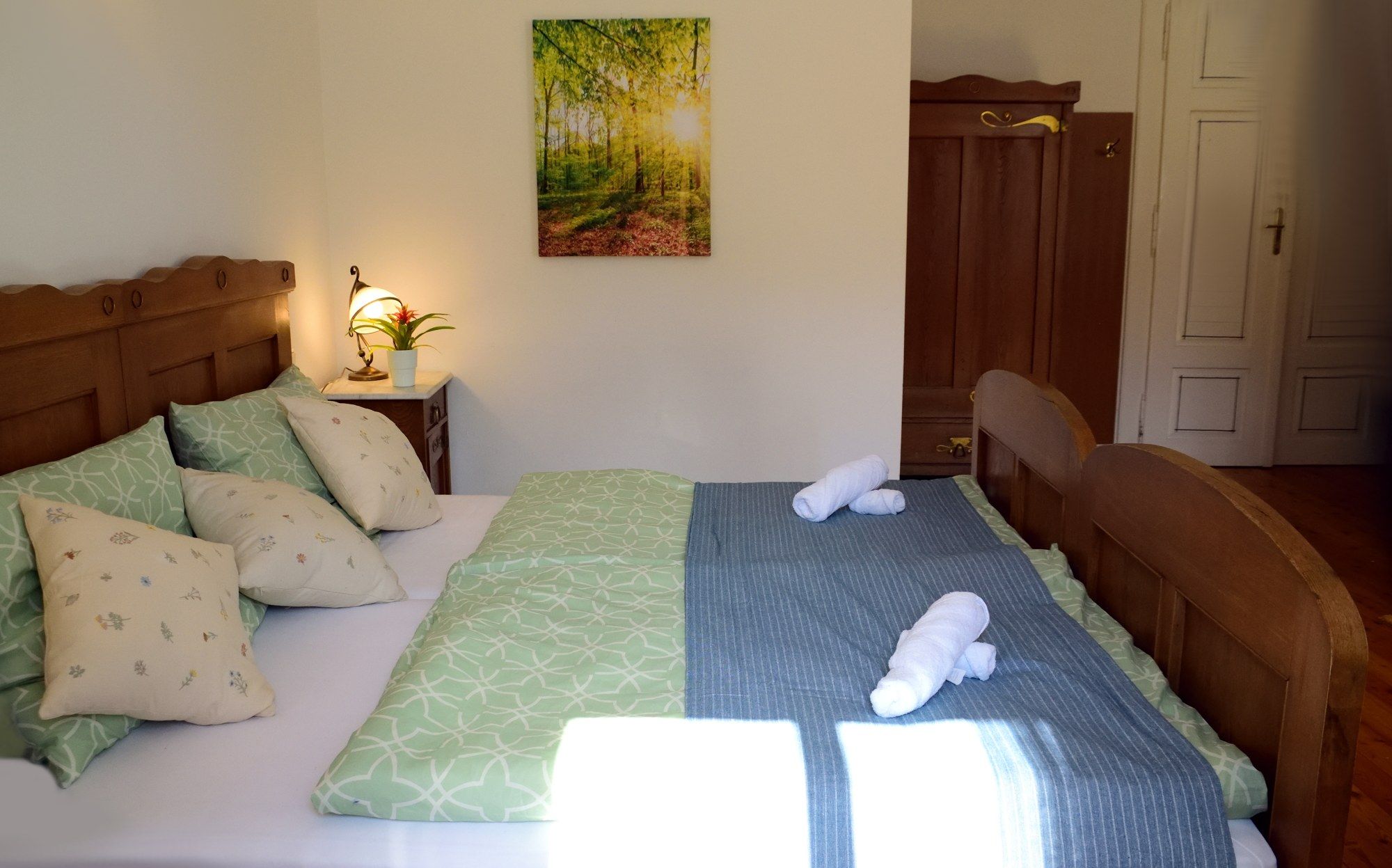 Gemütliches Doppelzimmer mit Holzmöbeln, grünem Bettzeug und einem Bild an der Wand.