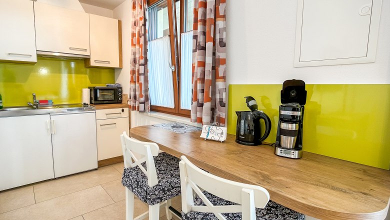 Moderne K&uuml;che mit gr&uuml;ner R&uuml;ckwand, wei&szlig;en Schr&auml;nken, Holztheke und Kaffeemaschine.