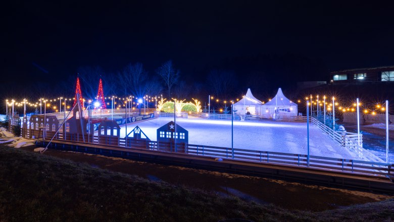 Beleuchteter Eislaufplatz bei Nacht mit dekorativen Lichtern und Zelten.