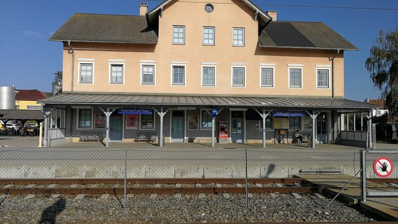 Bahnhof Hadersdorf am Kamp mit Gleisen im Vordergrund und einem gelben Geb&auml;ude im Hintergrund.