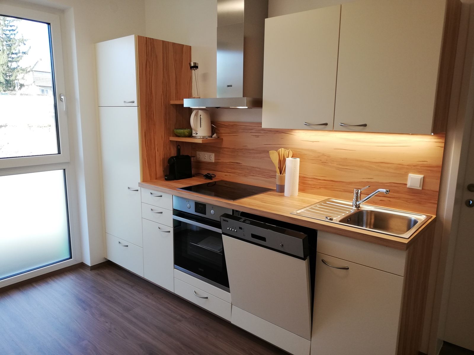 Moderne Küche mit weißen Schränken, Holzarbeitsplatte, Spüle und Elektrogeräten.