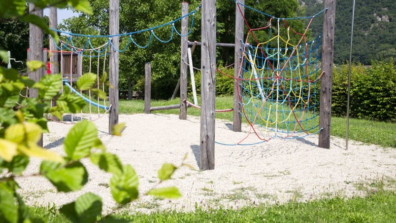 Ein Abenteuerspielplatz mit Kletterseilen und Holzmasten, umgeben von gr&uuml;ner Natur.