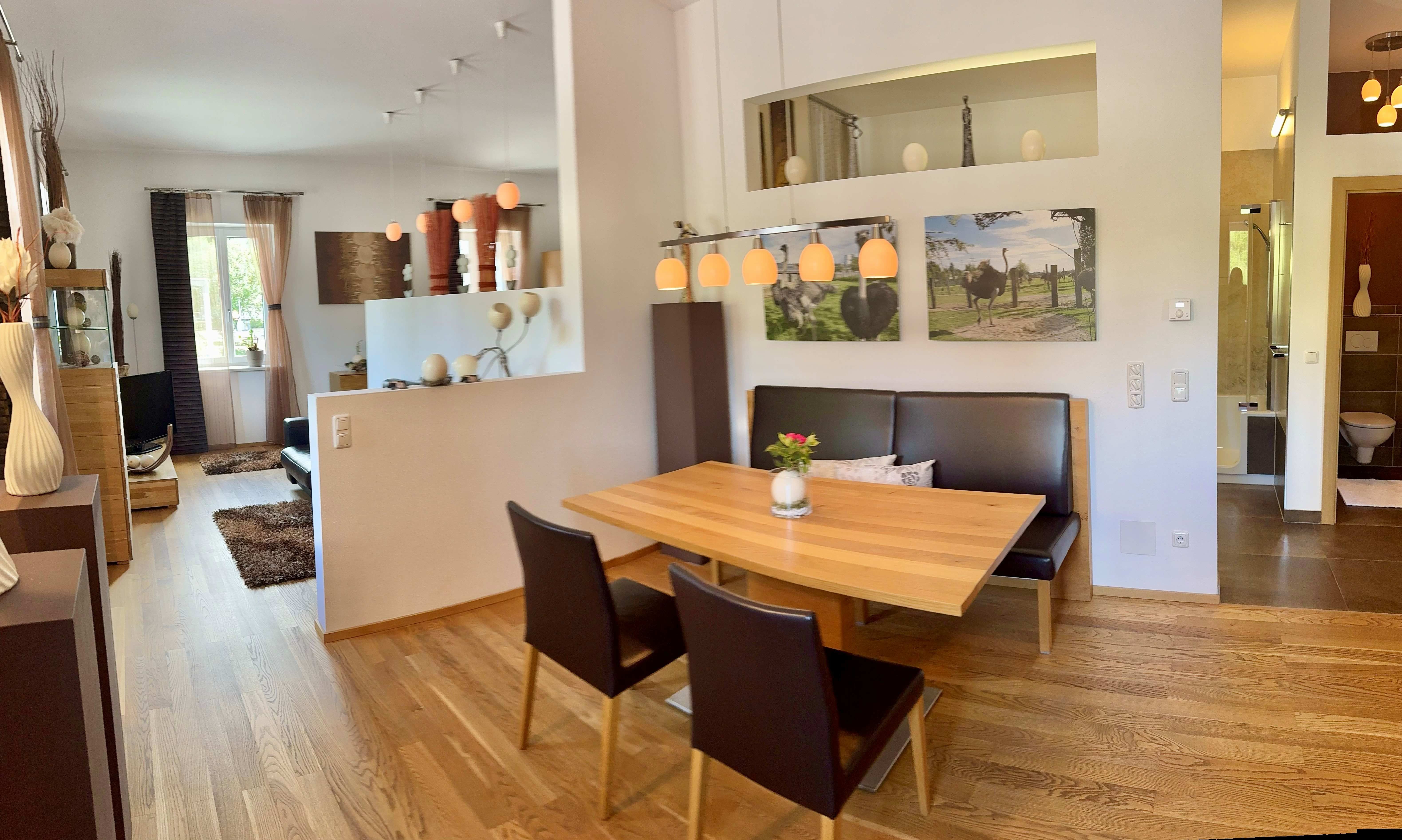 Modern eingerichtetes Wohnzimmer mit Esstisch, Stühlen und Dekorationen, darunter Bilder von Straußen.